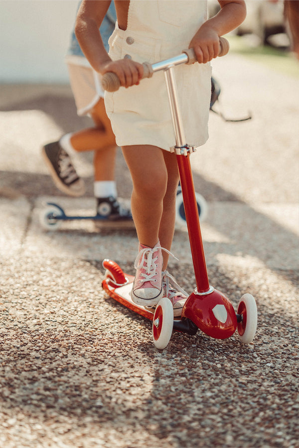 meisje stept buiten op rode kinderstep met 3 driewielen