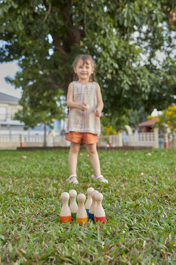 kindje speelt buiten in tuin met houten bowlingspel 