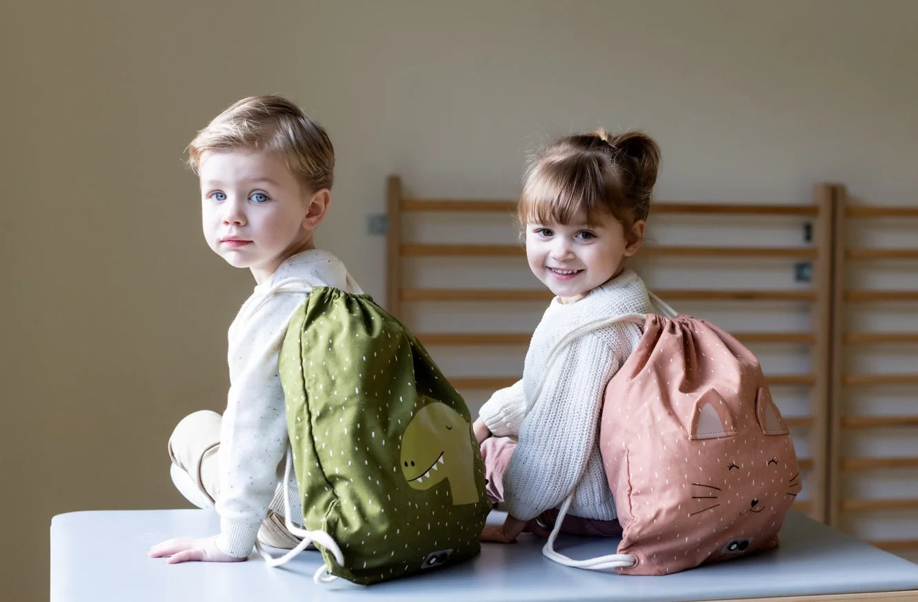 Twee kindjes zitten op een lint en kijken over hun schouder met een turnzak van trixie op hun rug